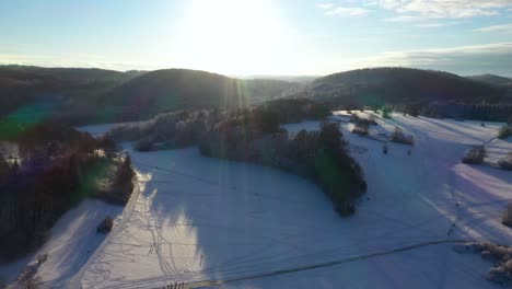 Stunning-aerial-panning-up-revealing-snow-covered-mountains,-forest-and-clear-sunny-sky-during-winter-in-Swabia,-Germany