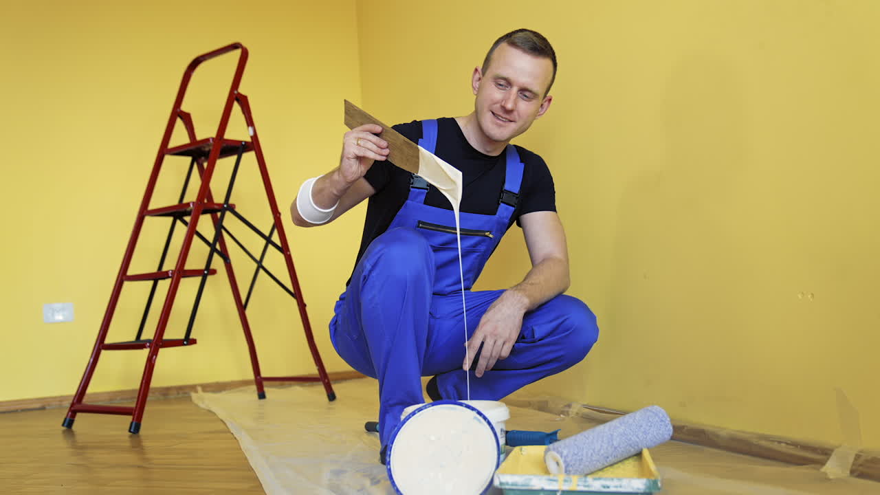 Repair and decorating walls in the house. Worker in blue overalls prepares color before painting walls in the room. Builder man working indoors. Makeover at home.