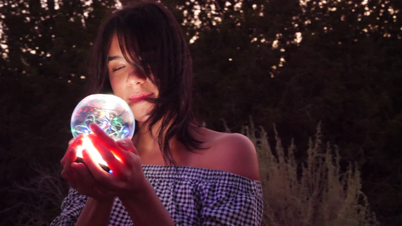 una hermosa mujer hechicera vagando en un paisaje de fantasía con una esfera espiritual mágica que brilla en la luz iluminada