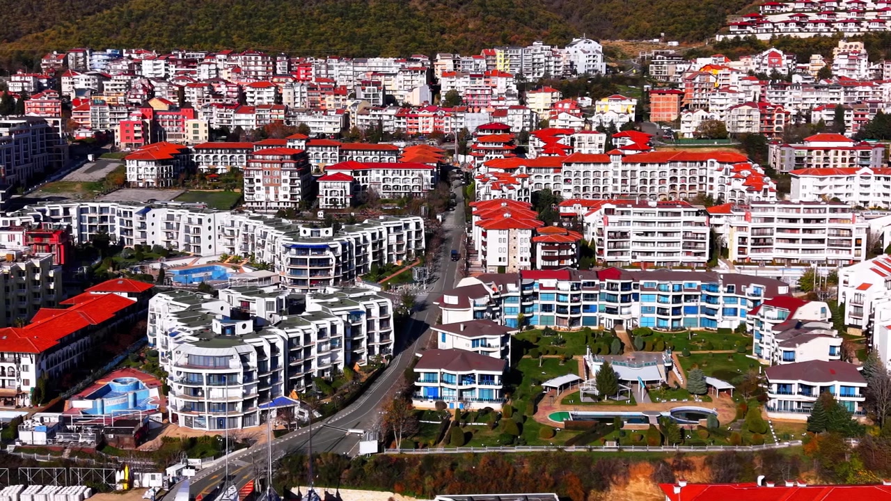 Bulgaristan'da konut apartman kompleksi. Kırmızı ve beyaz cepheli çok katlı binaların, havuzların ve arkasındaki ormanlık yamacın havadan görünümü
