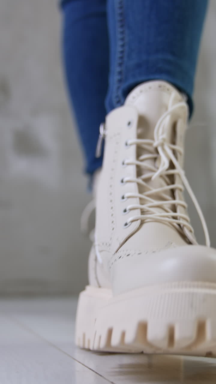 White leather army boots on a female wearing jeans. Woman demonstrating stylish footwear in the studio. Vertical video