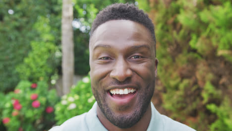 retrato de un hombre afroamericano sonriente mirando a la cámara en el jardín