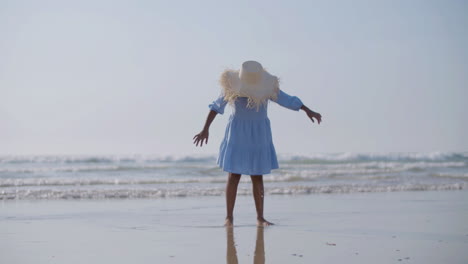 cute girl in straw hat jumping and laughing at seashore barefoot