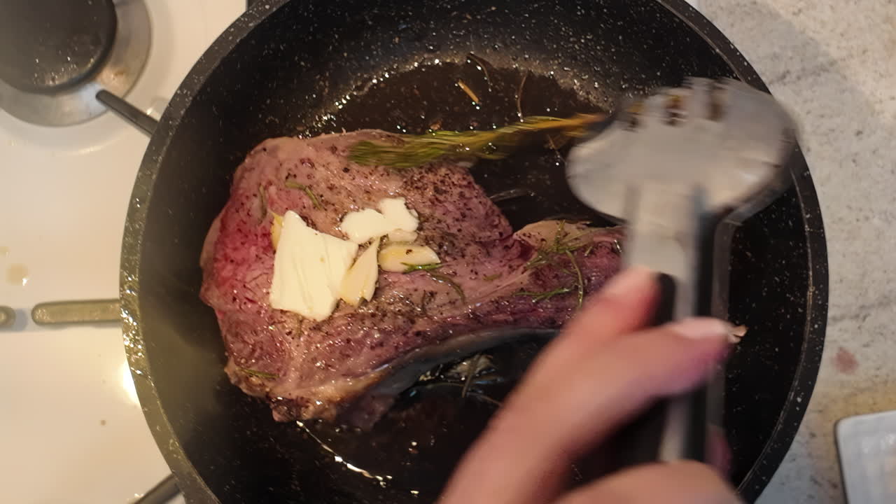 Cooking of a big red beef stake in a black pan with onion and rosemary