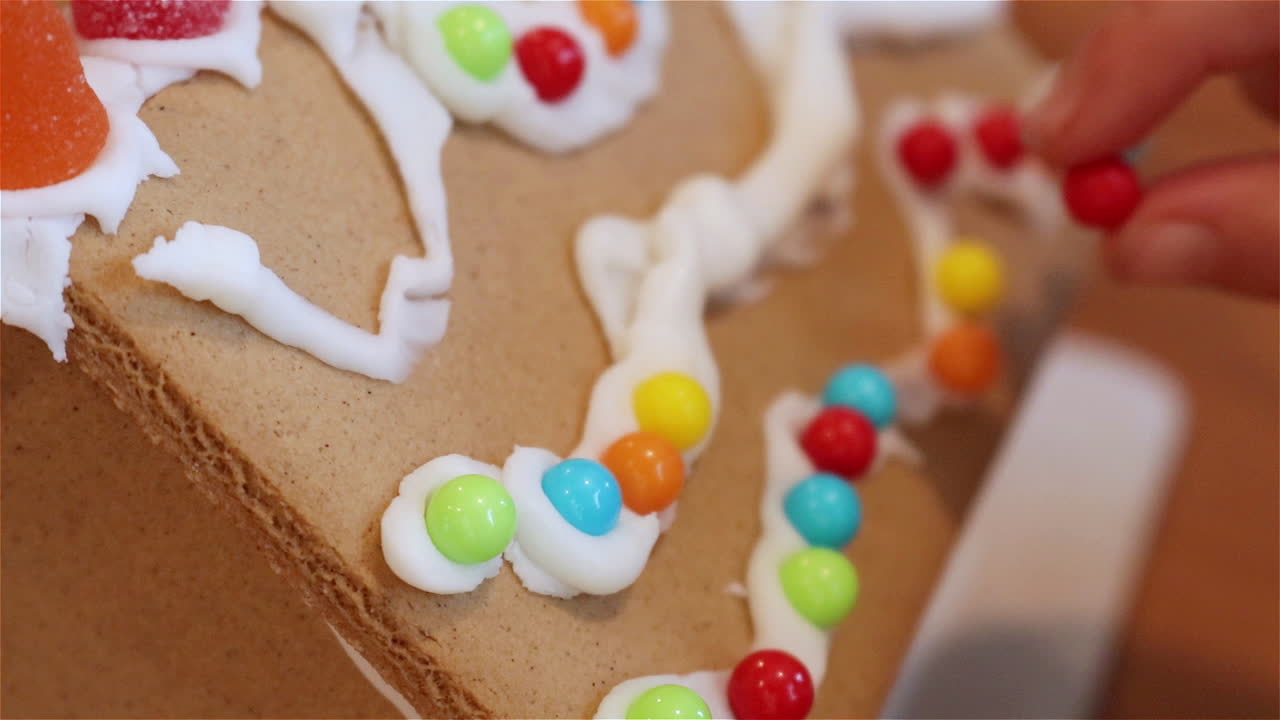 Young girl crafting a gingerbread house with small colorful candies