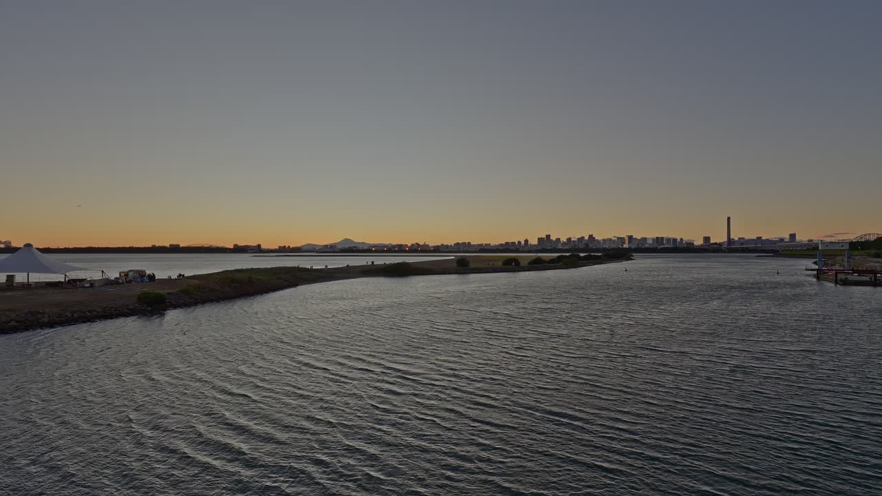 A wide panoramic shot of Tokyo Bay and the city skyline with a faint outline of Mount Fuji visible under a clear, warm twilight sky