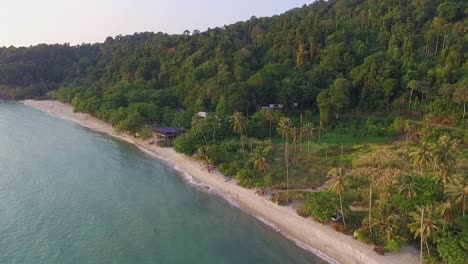 Tropical-Island-drone-dolly-trucking-shot-of-beach-with-lush-green-rain-forest-and-tropical-palm-trees-with-white-sand-beach-and-rocky-coastline