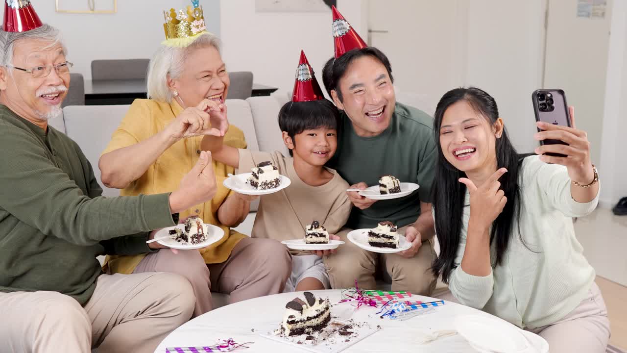 Joyful multigenerational Asian family celebrates birthday with cake, party hats, and smiles indoors