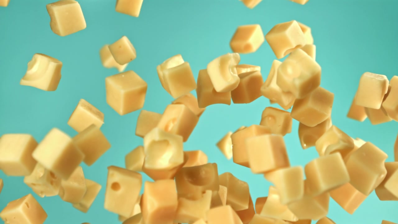 Dés de fromage tombant au ralenti sur un fond sarcelle