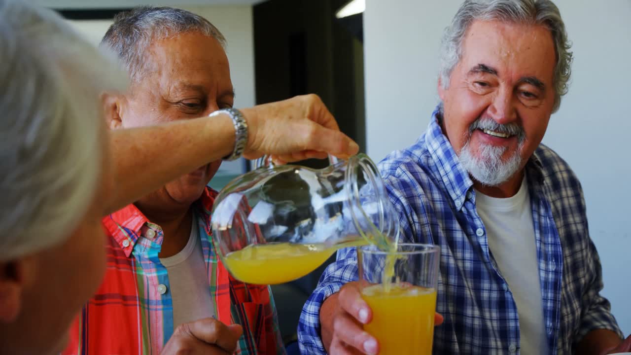 mujer mayor vertiendo jugo en un vaso a su amiga 4k