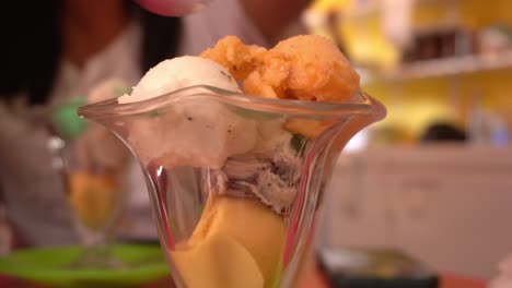 primer plano de varias bolas de helado naranja, amarillo y blanco en una taza de vidrio en d