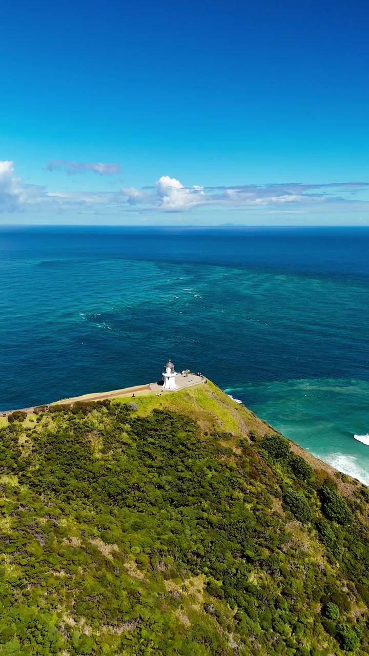 Verticale, aerea: Faro di Cape Reinga, Mar di Tasman e Oceano Pacifico durante il giorno a Cape Reinga, Nuova Zelanda, ripresa aerea introduttiva con drone.