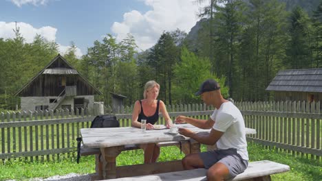 two hikers enjoy a relaxing outdoor lunch at a wooden picnic table in a scenic mountain setting