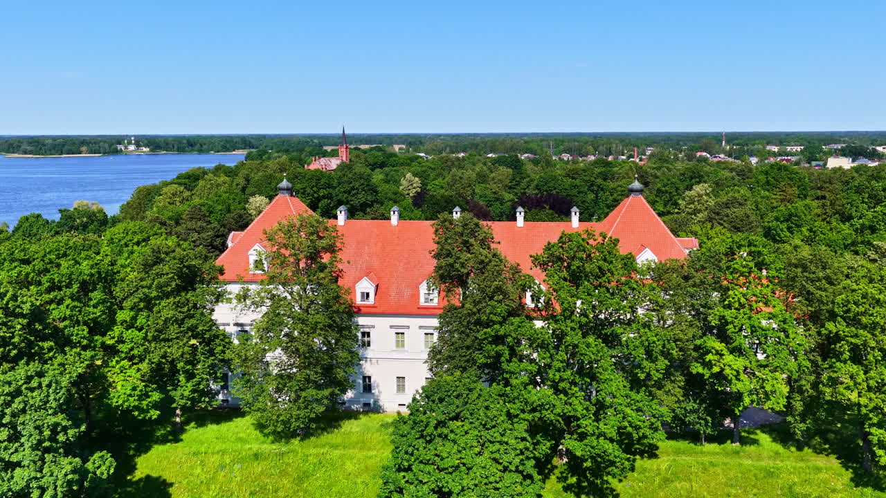 Aerial view of Biržai Castle with red roof surrounded by lush green forest in Lithuania