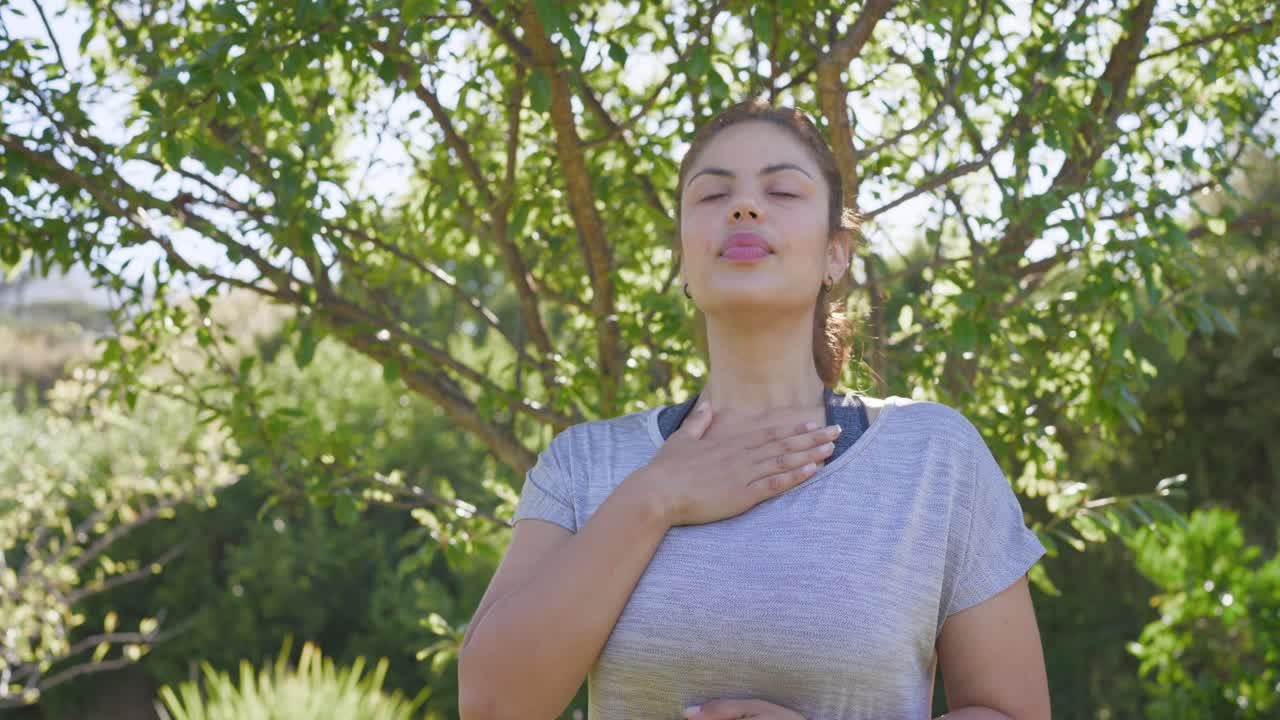 Mulher afro-americana colocando as mãos no peito, praticando respiração abdominal no jardim, usando sutiã esportivo, acalmando-se.