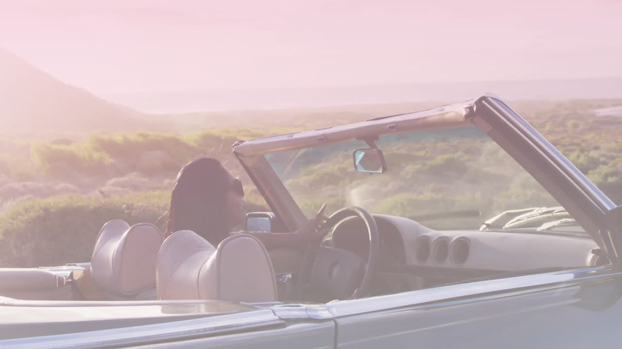 animación de sombra de luz sobre mujer biracial conduciendo un coche en la orilla del mar