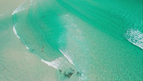 vista aérea en cámara lenta de las claras olas del océano lavando suavemente sobre una playa de arena con aguas pacíficas y serenas
