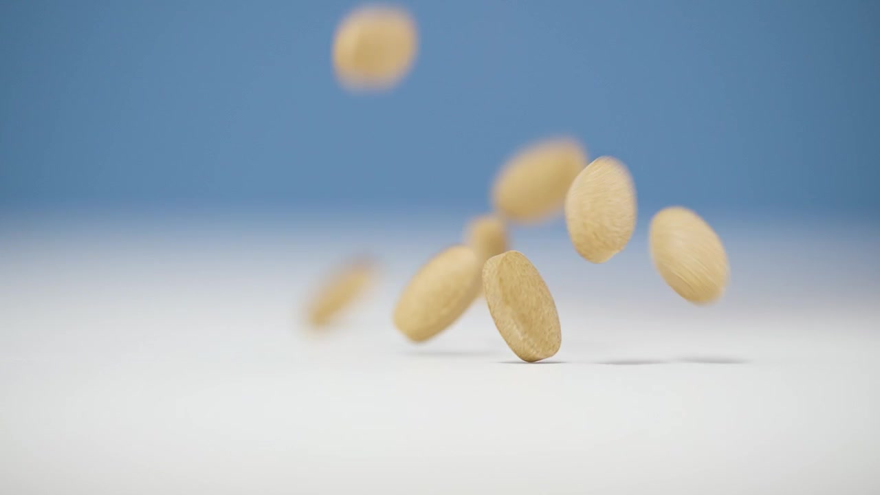 Primo piano di pillole circolari beige che cadono su una superficie bianca su uno sfondo blu sfocato
