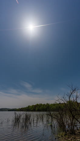 a vertical timelapse video of a total solar eclipse recorded from start to finish, with the darkened sun in a clear daytime sky above a calm lake.