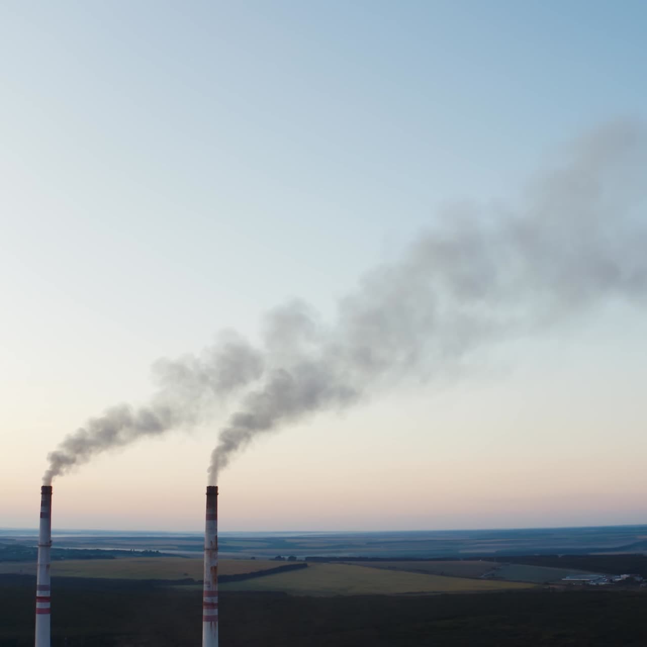 Two pipes with smoke on the fields background. Industrial pipes with smoke among fields and forests in the evening.