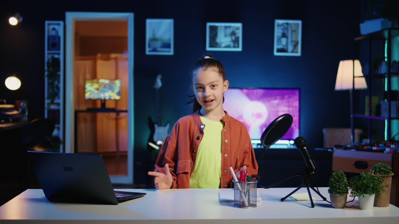 Bambino felice seduto alla scrivania in un appartamento illuminato da luci al neon blu, che discute argomenti con un giovane pubblico.