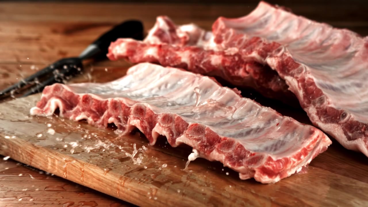 Slow Motion Water Splashing on Raw Pork Ribs on a Wooden Board