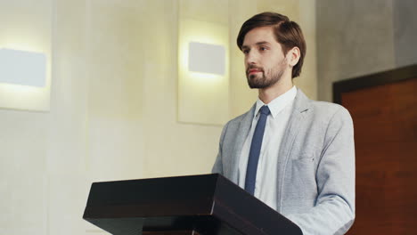 close-up view young caucasian businessman in formal clothes on a podium looking at the camera and smiling in a conference room