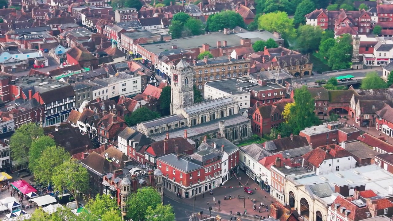 Flygfoto med drönare över St Thomas Church i Salisbury, omgiven av historiska byggnader, takåsar, gator och grönska i stadskärnan.