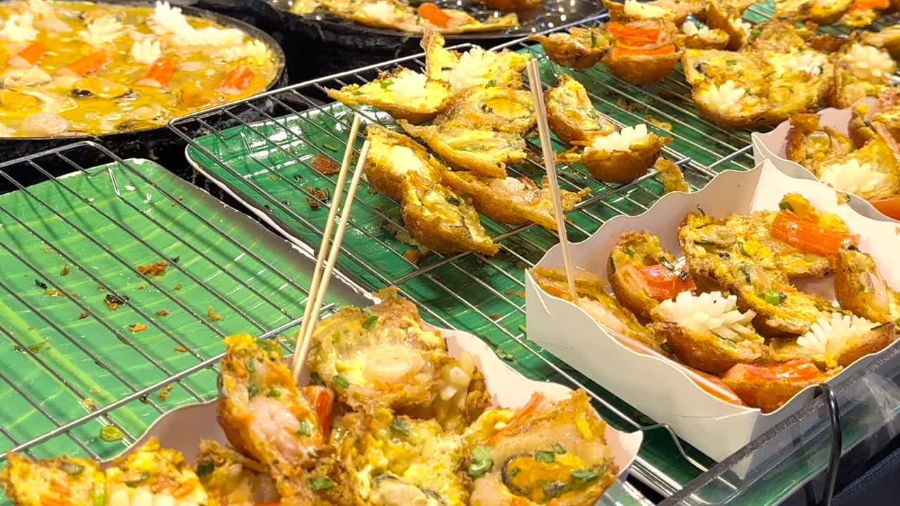 Jarak dekat omelet seafood goreng renyah yang disajikan dalam nampan kertas di pasar yang ramai