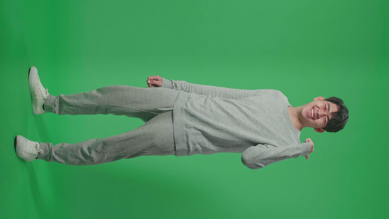 Full Body Of Side View Smiling Asian Man Pointing To The Back Behind By Thumbs Up While Standing In Front Of Green Screen Background
