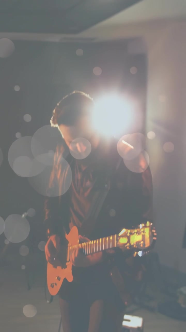 Video verticale: Uomo in pelle che strimpella e cambia accordi su una chitarra gialla in studio, dopo un segnale luminoso.