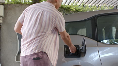 charging electric car at home, man plugging in vehicle in garage