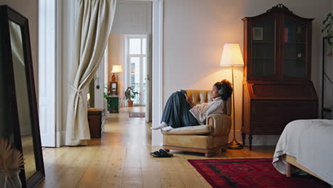 calm girl relaxing armchair home. curly hair brunette listening headphones music