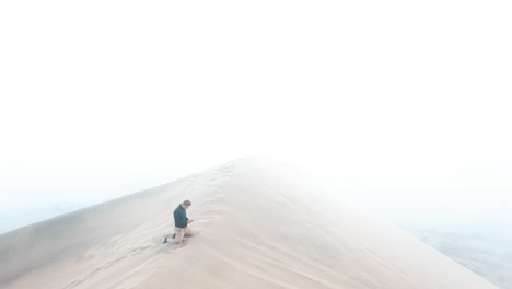 a man kneeling on a dune. huacachina, peru, desert, drone aerial