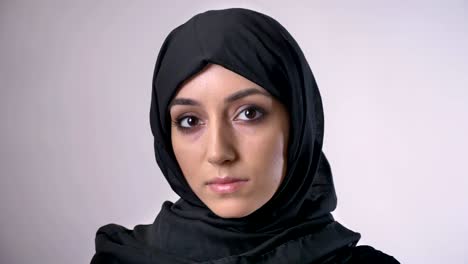 una joven musulmana seria con hijab está mirando a la cámara, fondo gris