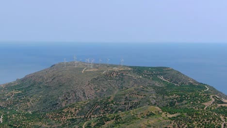 drone view above mountain approaching wind turbines in distance, blue ocean water background unobstructed view