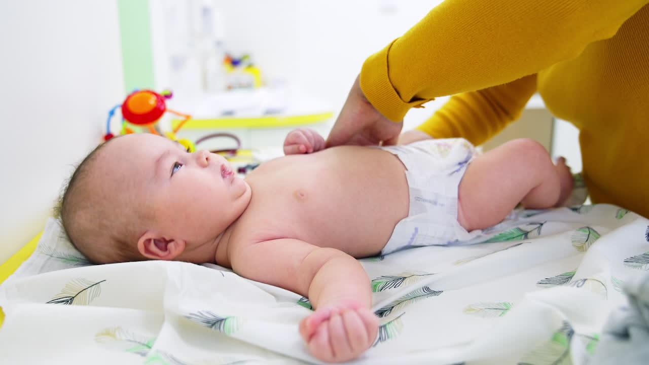 Mother's hands touch up baby's diaper. Infant boy lying still and calm after the doctor's check-up. Side view. Close up.