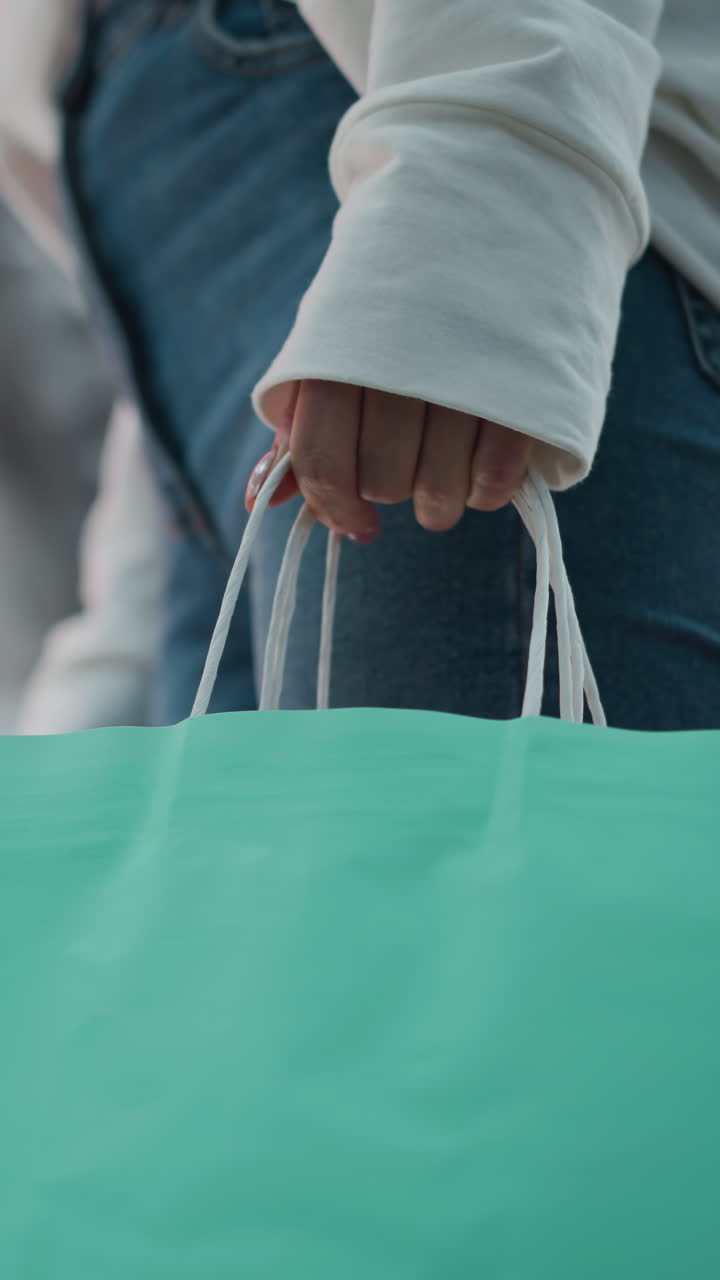 vista lateral de una mujer de pie con una bolsa de compras de menta balanceándose suavemente, con una camiseta blanca casual y vaqueros, con un maniquí borroso y un fondo rojo vibrante