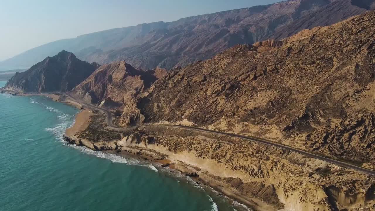 driving vehicle on the coastal road alongside the rock mountain beach in sunset time the wind erosion spectacular multilayer landscape in background the marine water sport tourism attraction in Iran