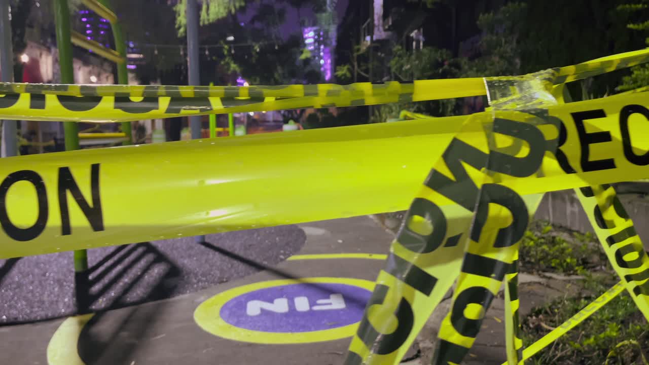 A close-up of caution tape reading “Precaución” in a playground setting, illuminated by urban street lights during the night. Location: Guatemala City, Guatemala