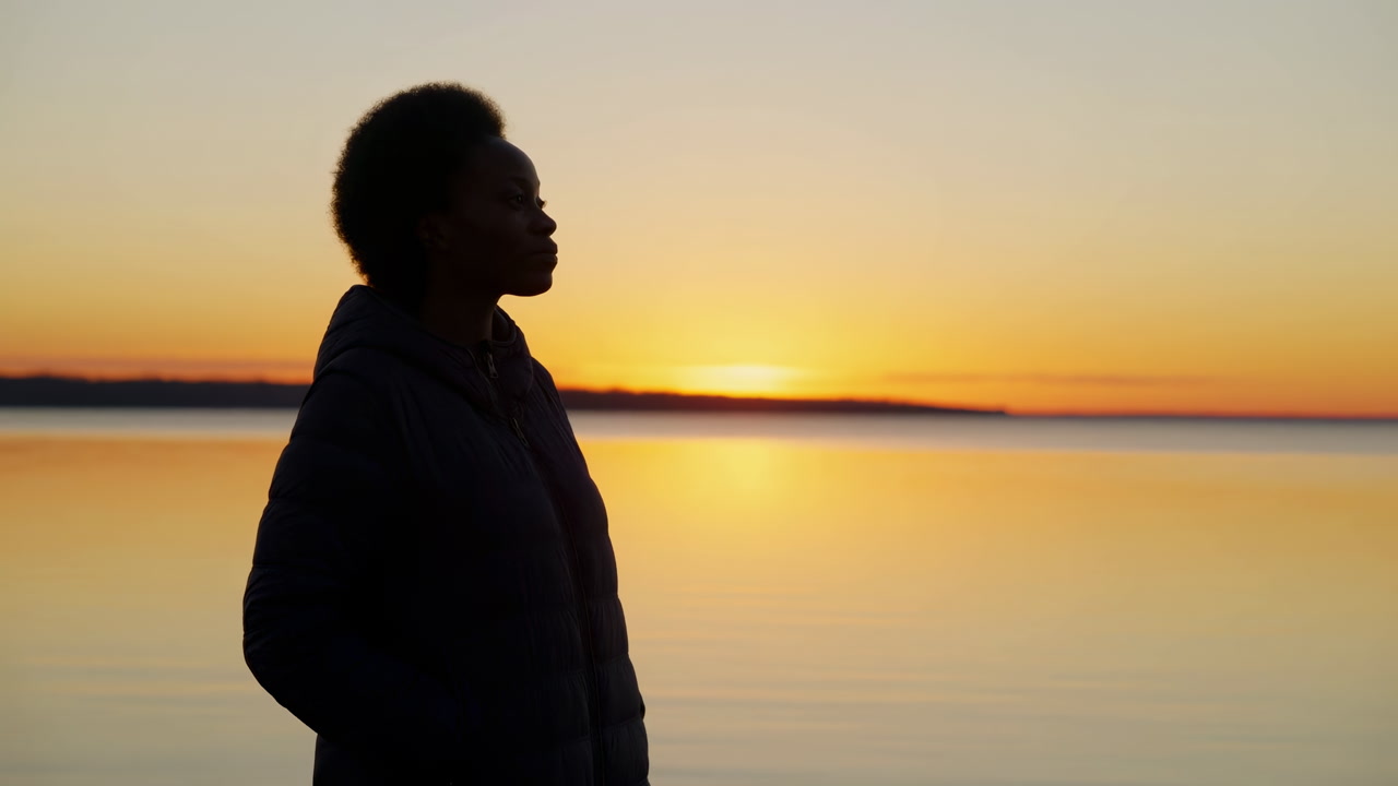 Black Woman Silhouette At Sunset Lake, Quiet Waterfront Scene With Reflective Woman Standing Facing Horizon,