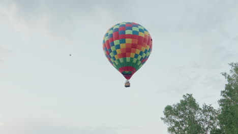 trip with people drifting in vibrant checkered hot air balloon over open sky at sunset while distant second balloon appears on horizon adding depth to serene aerial exploration