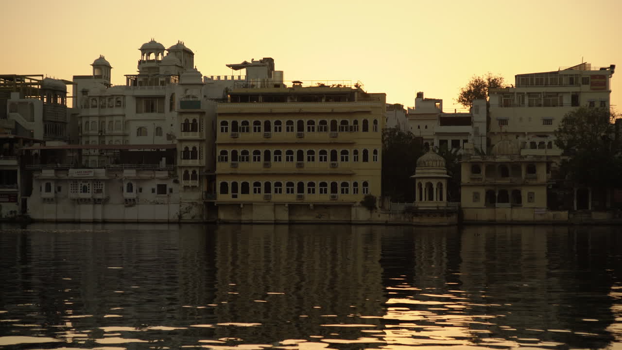 a medida que el sol se sumerge debajo del lago pichola en udaipur, india, los graciosos patos se deslizan a través del agua, complementando el sereno telón de fondo de la impresionante arquitectura, lo que resulta en una vista cautivadora.