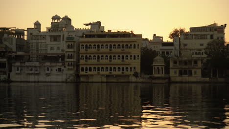 Mientras-El-Sol-Se-Esconde-Bajo-El-Lago-Pichola-En-Udaipur,-India,-Elegantes-Patos-Se-Deslizan-Por-El-Agua,-Complementando-El-Sereno-Telón-De-Fondo-De-Una-Impresionante-Arquitectura,-Lo-Que-Da-Como-Resultado-Una-Vista-Cautivadora.