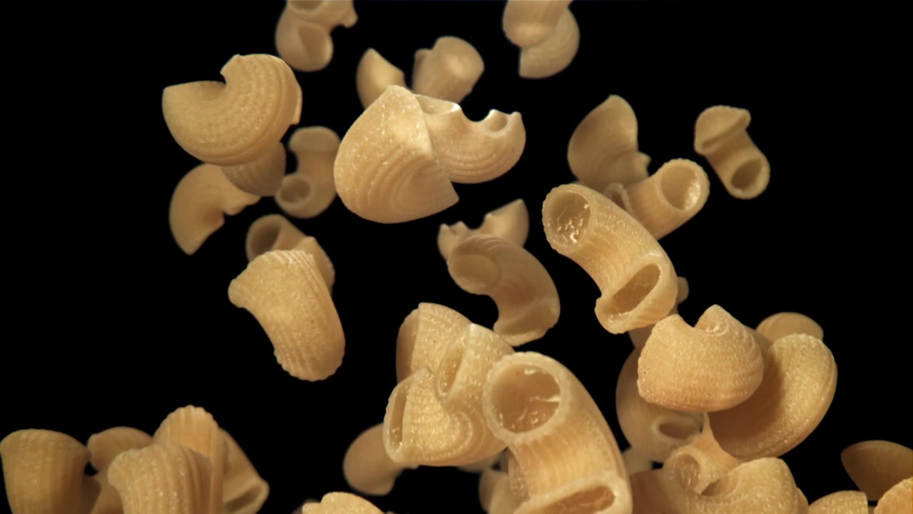 Pasta maccheroni secca che cade su sfondo nero al rallentatore