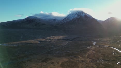 Glencoe-valley-with-snow-capped-mountains-and-river,-sunlight-casting-shadows,-serene-landscape,-aerial-view