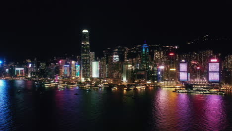 hong kong night aerial view of hong kong island, boats sailing on victoria harbour. panning backwards. central financial district hub