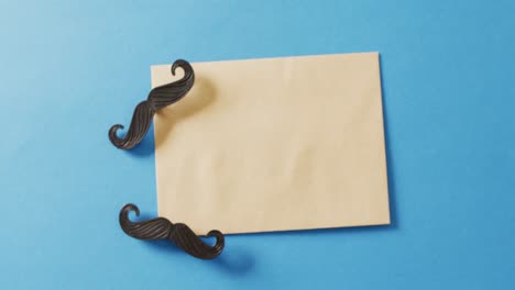 Video-of-two-false-moustaches-and-yellow-envelope-with-copy-space-on-blue-background