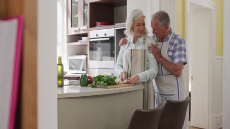feliz pareja caucásica mayor en casa en la cocina usando delantales