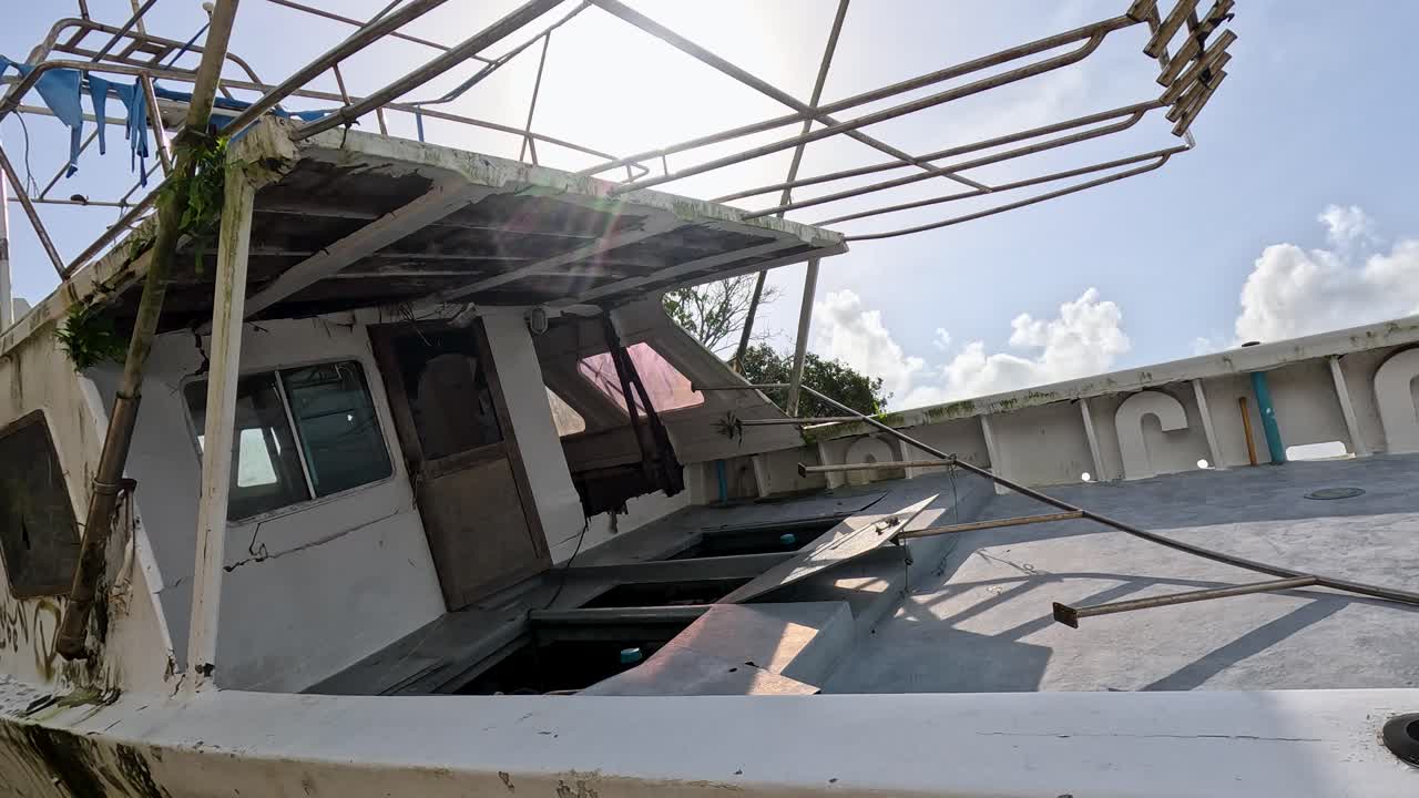 A beached, weathered fishing boat sits under a clear sky with harsh sunlight, captured in a slow upward camera tilt on Ko Phayam, Thailand